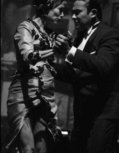 Black and white photograph of a tango couple in a close embrace, the woman in a lace-trimmed dress and the man in a tuxedo