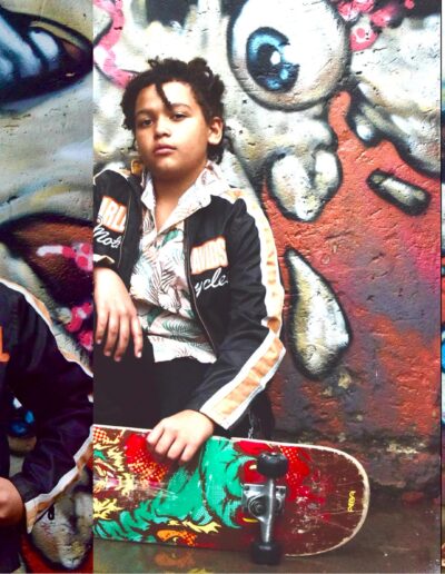 Colour triptych of a young person in a motorcycle jacket and tropical shirt posing with a skateboard in front of graffiti