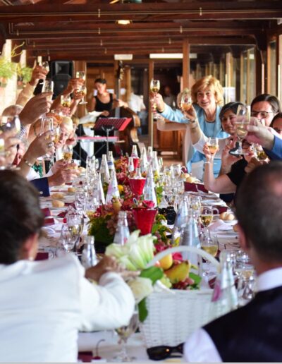 Colour photograph of wedding guests raising their glasses in a toast along a long, flower-filled banquet table