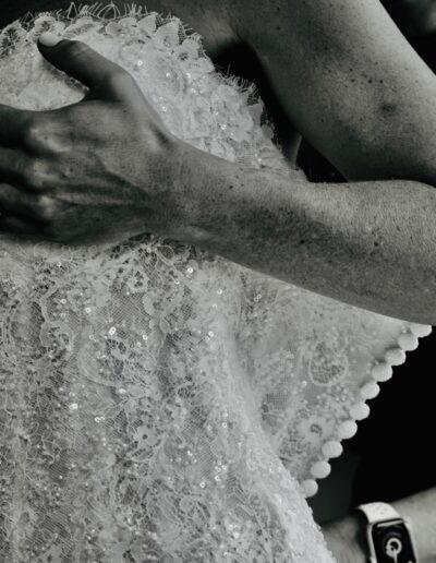 Black and white close-up of hands adjusting the beaded lace bodice of a wedding dress as the bride is helped into it