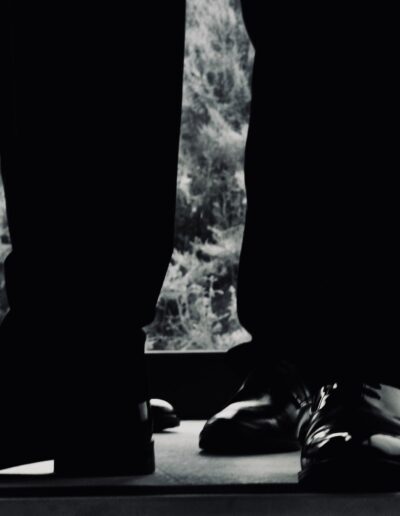 Black and white silhouette of groomsmen's polished shoes and dark trousers standing in front of a window